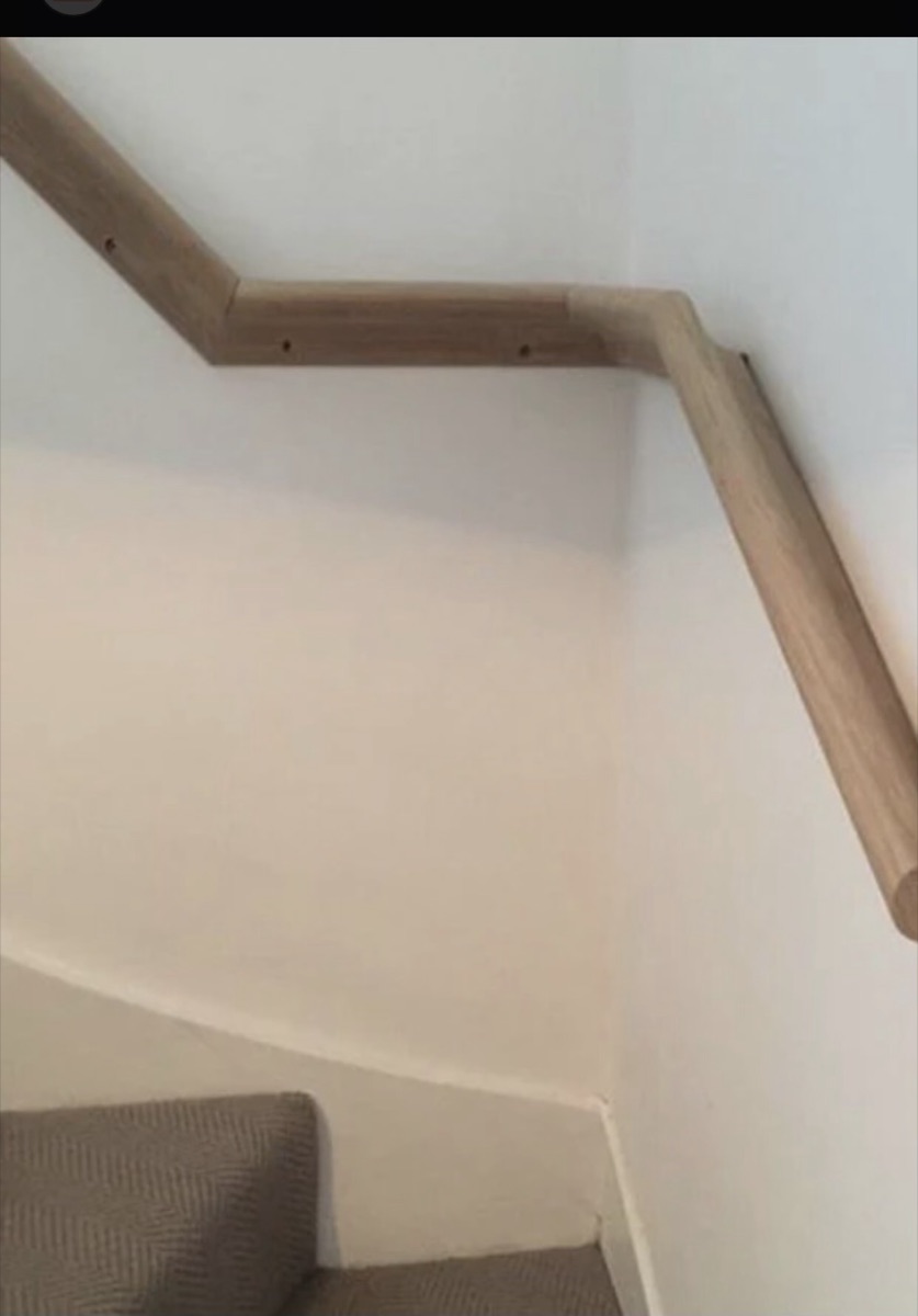 Curved wall-mounted solid oak handrail following a turning staircase