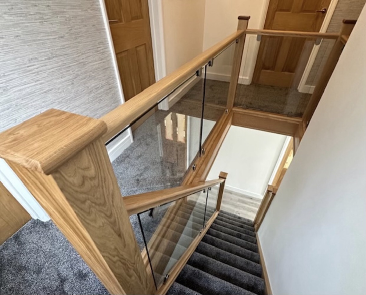 Oak and glass landing balustrade viewed from above over a granite-floored hallway