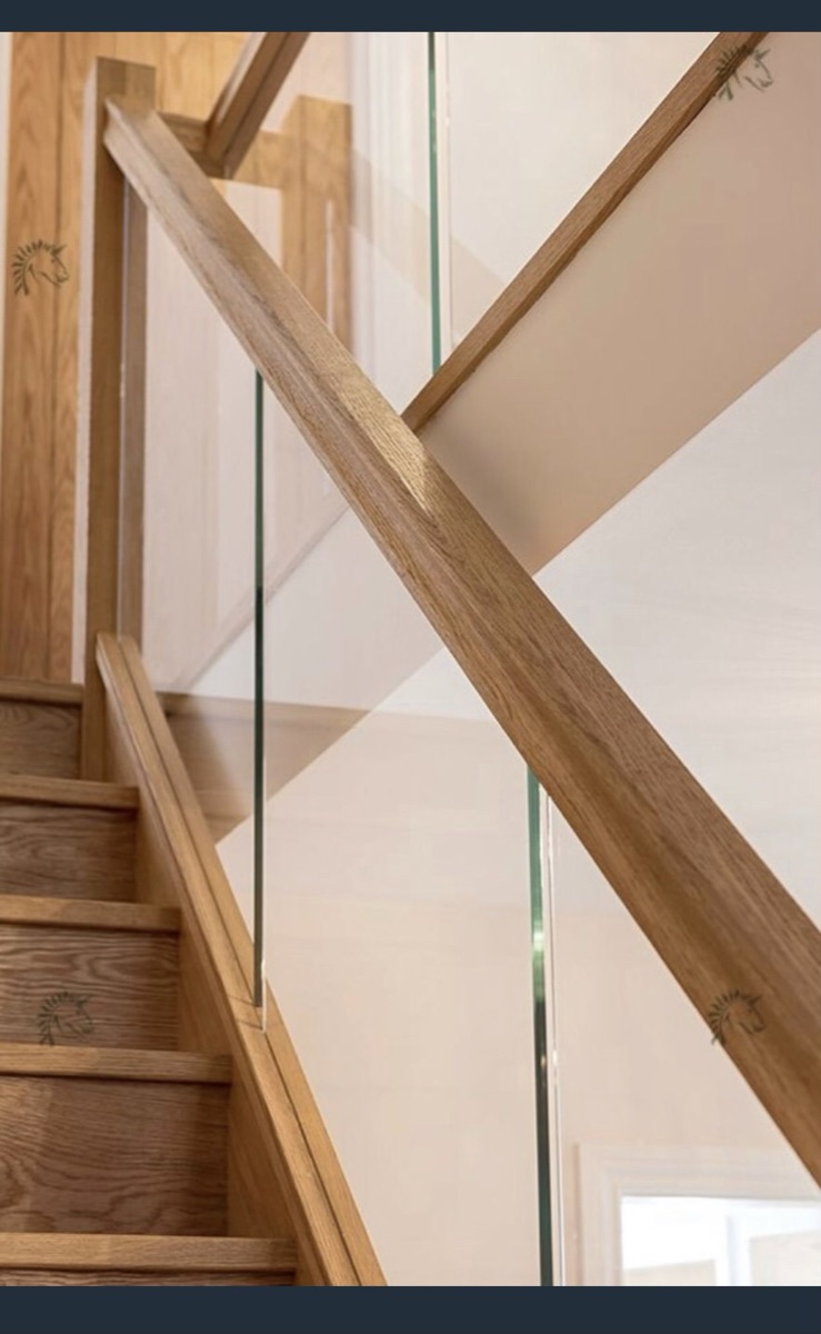 Close detail of an oak handrail meeting a raked frameless glass balustrade